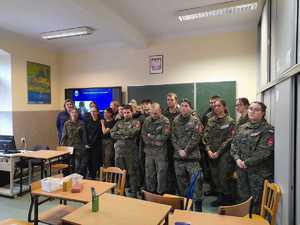 Zdjęcie grupowe. Uczniowie wraz z policjantkami oraz Rektorem Uczelni na tle klasy szkolnej.