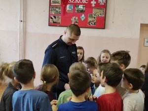 Policjant wśród otaczającej go grupy dzieci. Zdjęcie na korytarzu szkolnym.